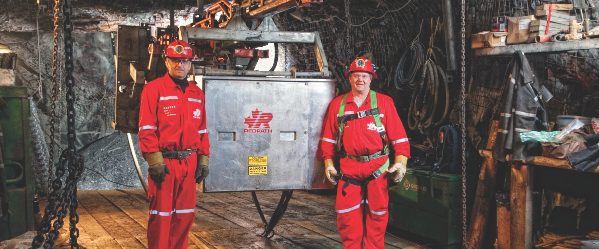 Two Redpath employees, dressed in safety gear, performing in-house repairs on a mechanized raise climber.